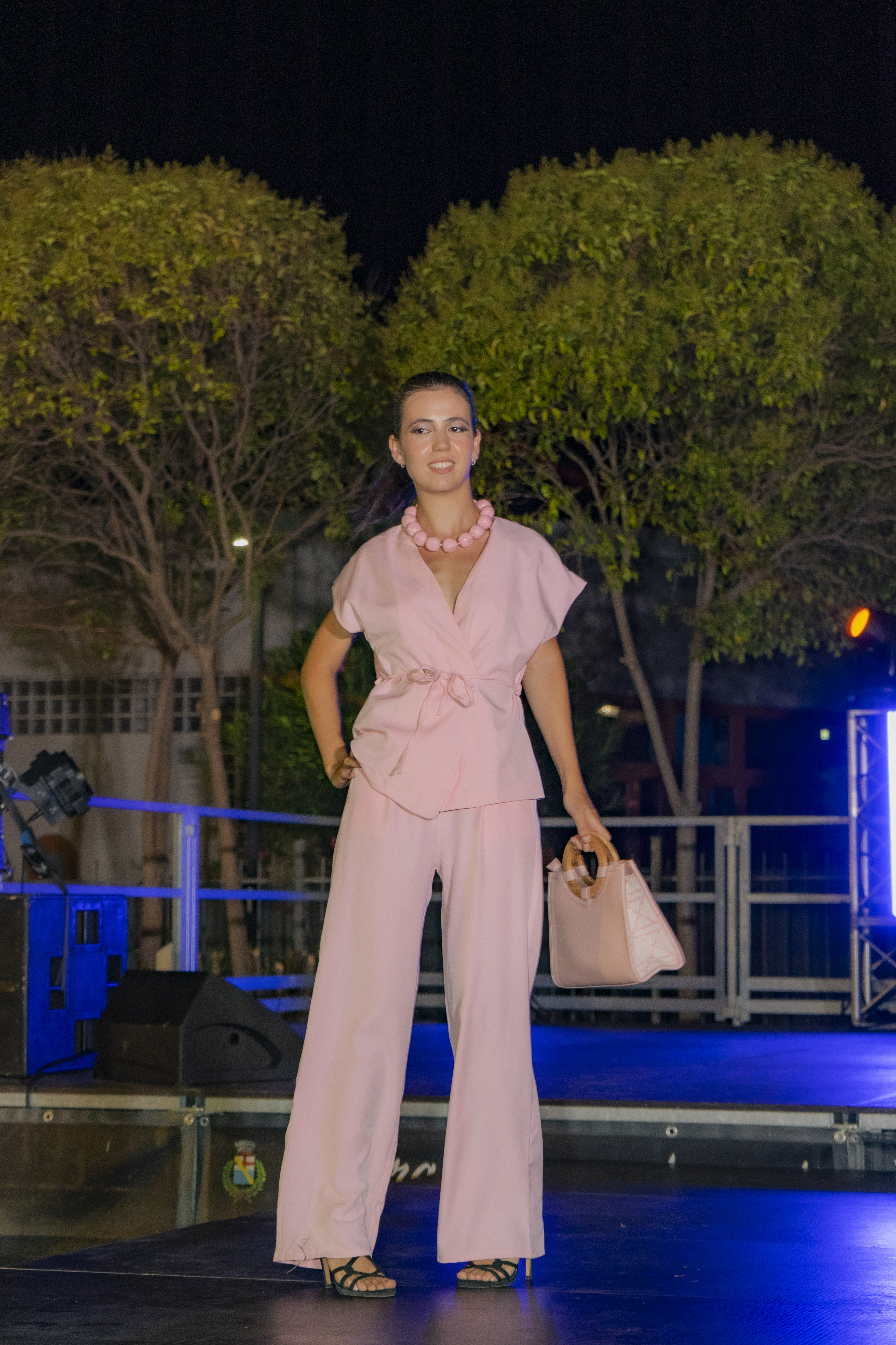 Modella in completo rosa sulla passerella con collana e borsa gialle